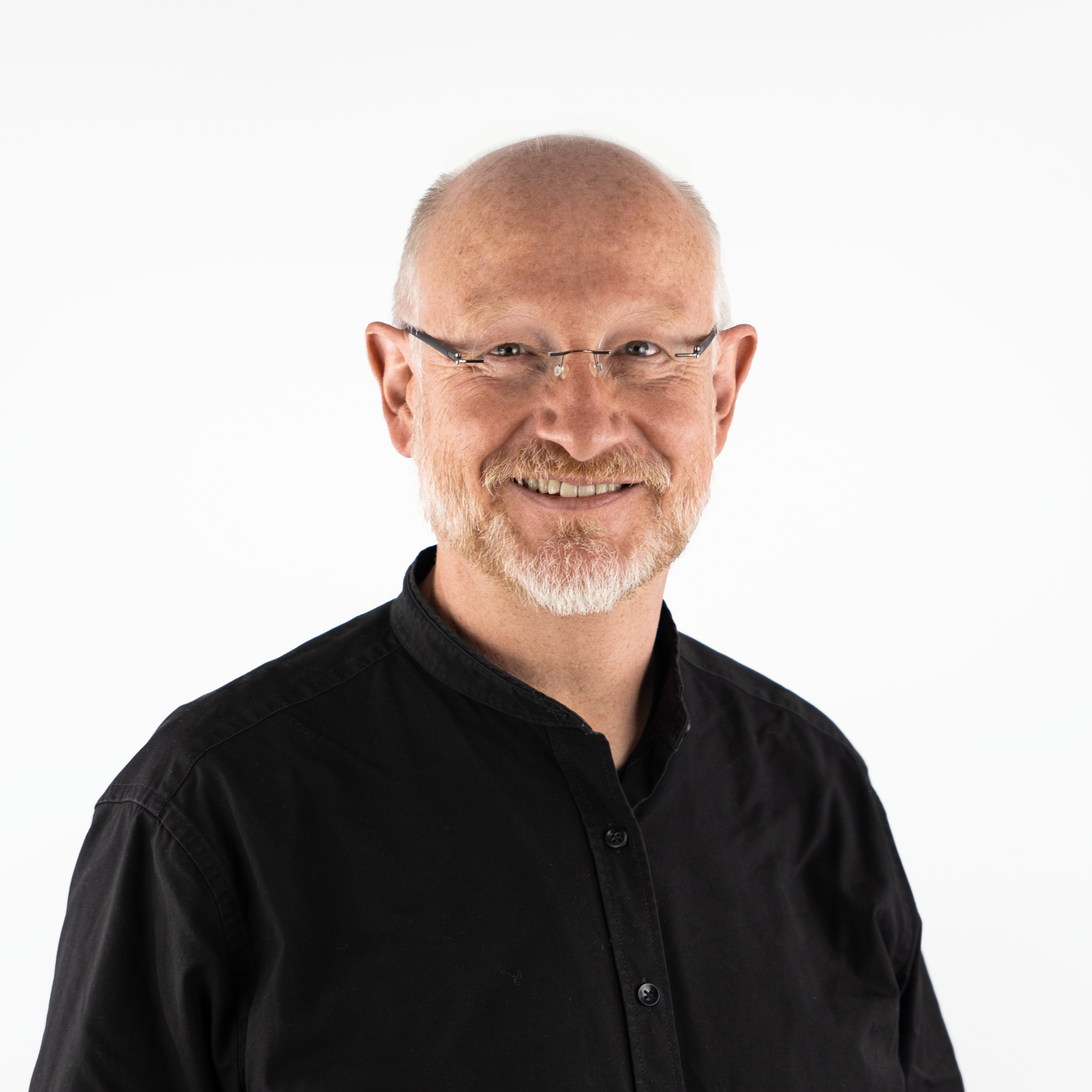 Porträt von Björn Hommert: ein freundlich lächelnder Mann mittleren Alters mit Brille, Bart und Glatze in einem schwarzen Hemd.