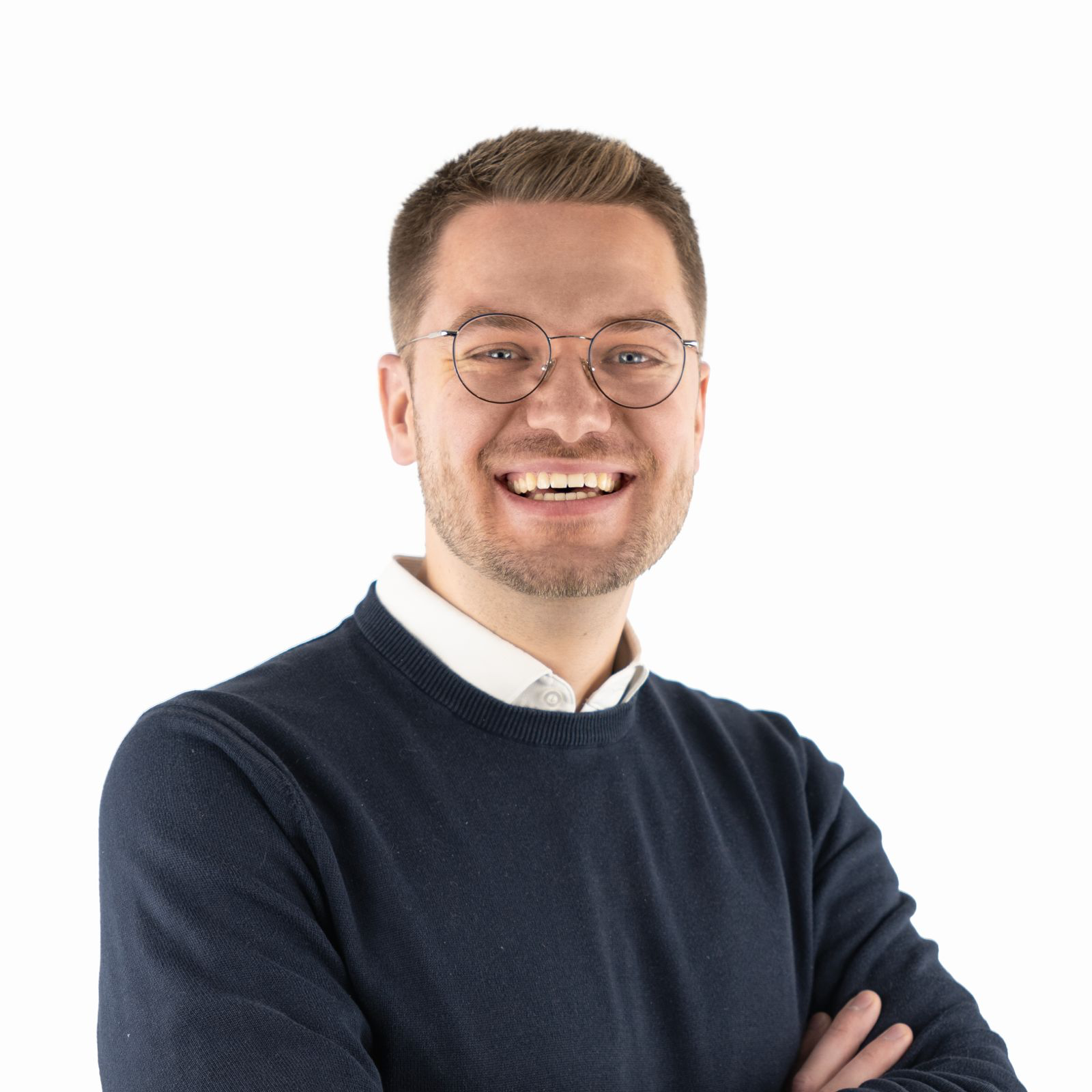 Porträt von David Jahn: Ein freundlich blickender Mann mit Brille, kurzen braunen Haaren und Bart. Er trägt einen dunkelblauen Pullover über einem weißen Hemd und hat die Arme verschränkt. Der Hintergrund ist weiß.