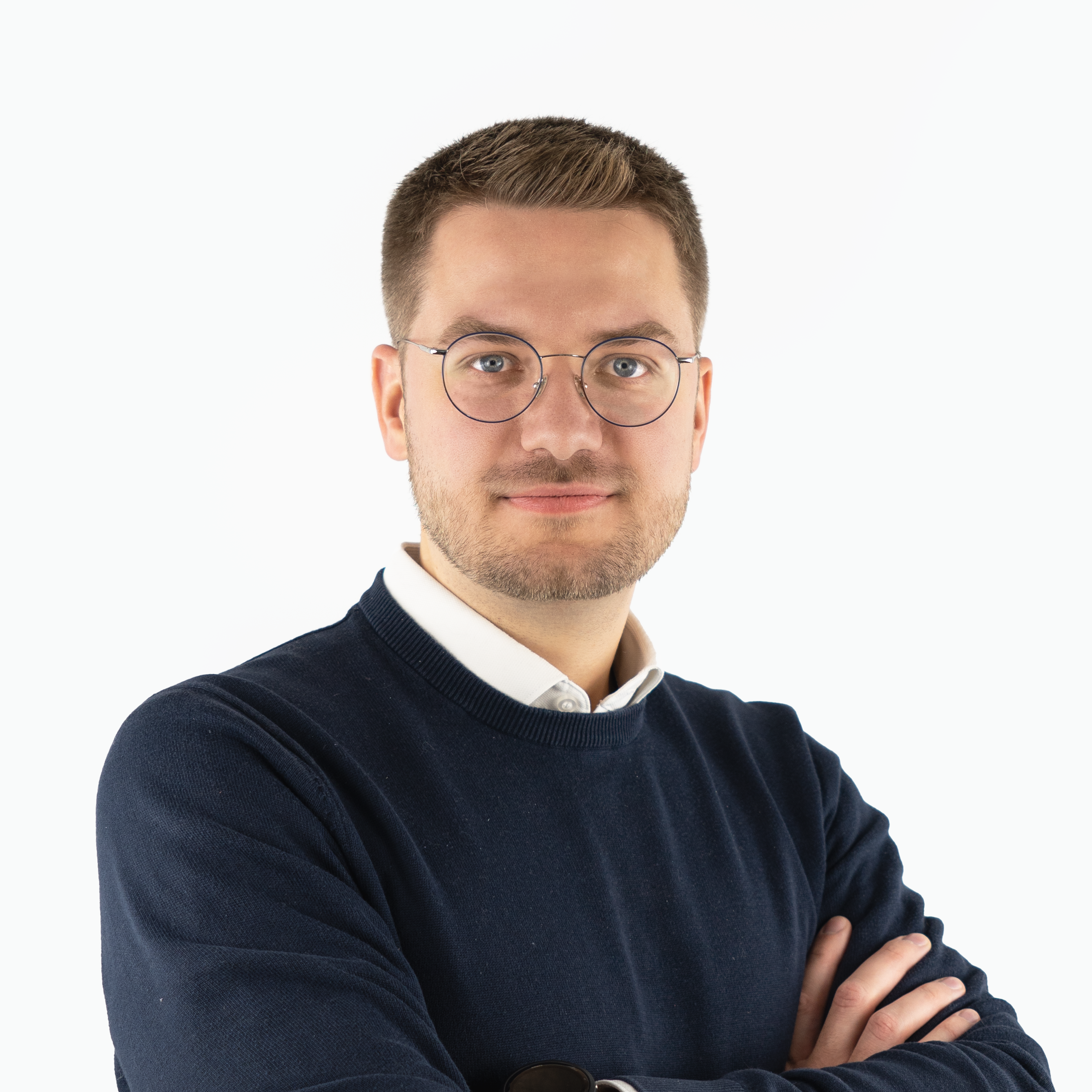 Porträt von David Jahn: Ein freundlich blickender Mann mit Brille, kurzen braunen Haaren und Bart. Er trägt einen dunkelblauen Pullover über einem weißen Hemd und hat die Arme verschränkt. Der Hintergrund ist weiß.