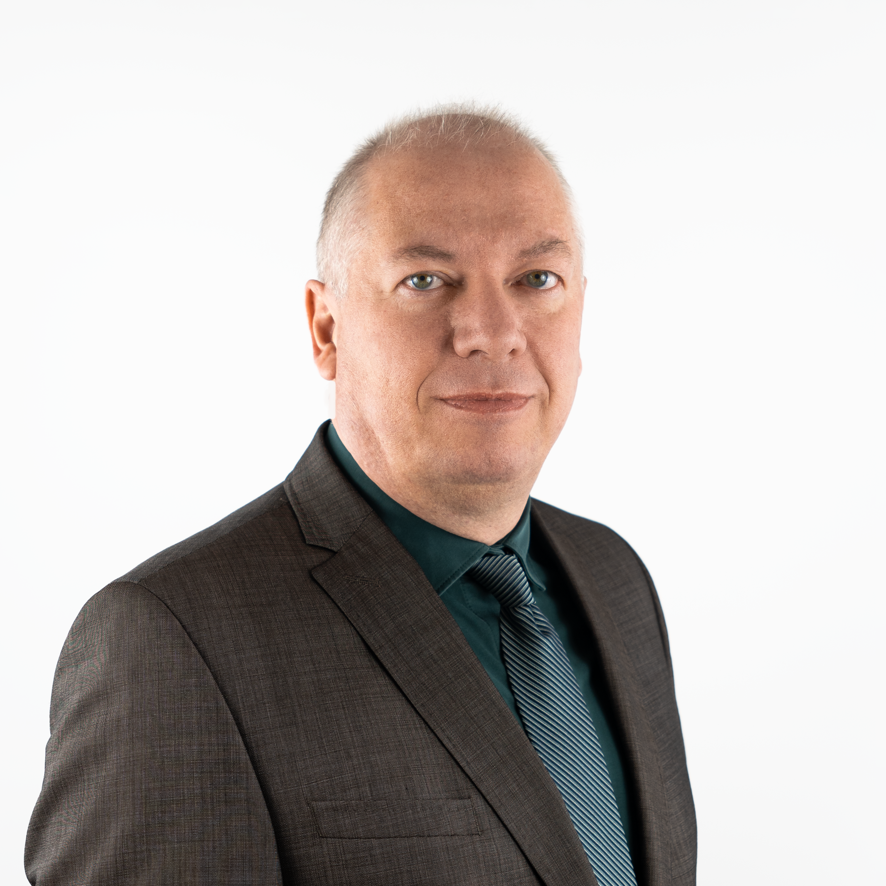 Porträtfoto von Jens Kreipl, einem Mann mittleren Alters mit kurzen, grauen Haaren. Er trägt einen dunklen Anzug, ein petrolfarbenes Hemd sowie eine blau-weiß gestreifte Krawatte und blickt freundlich in die Kamera.