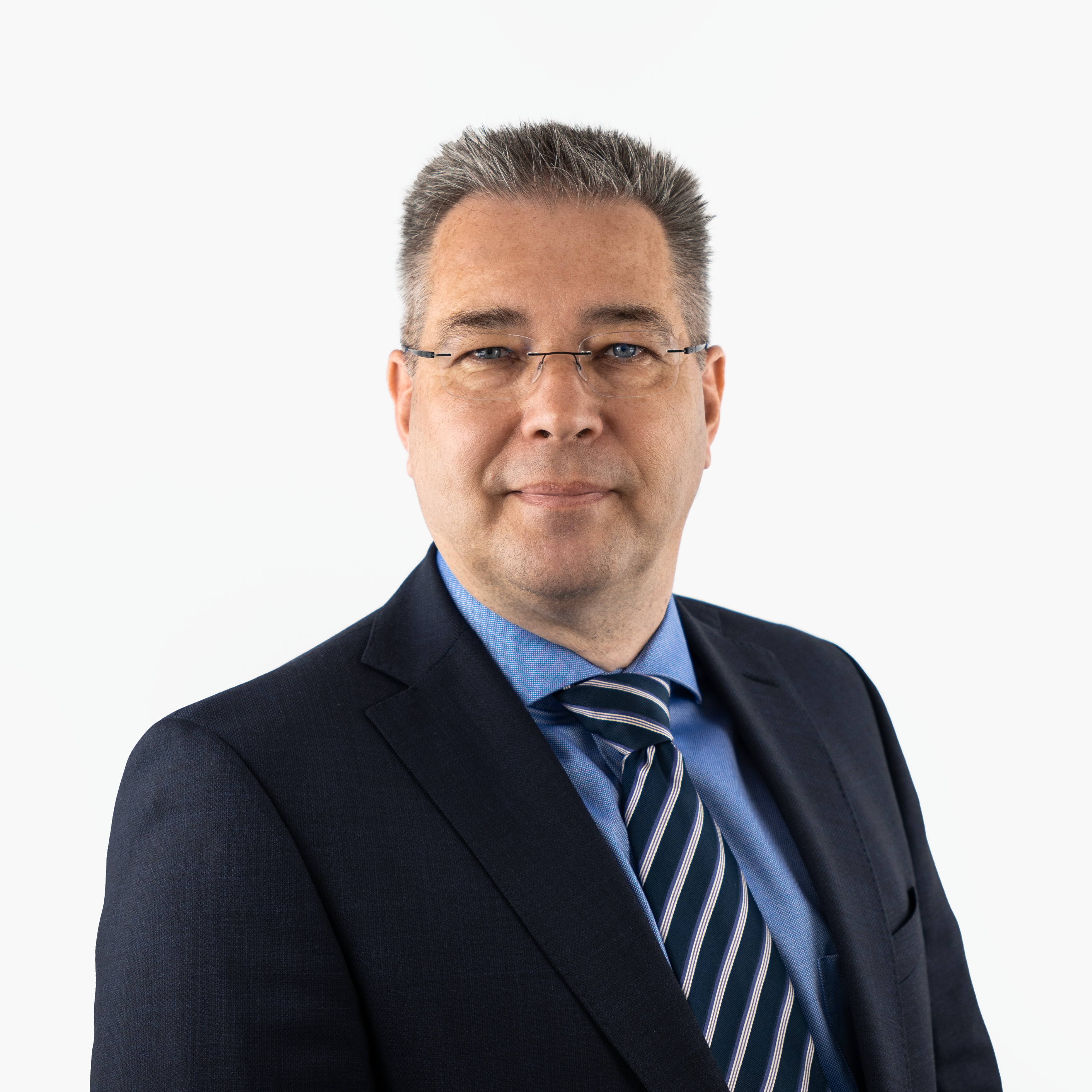 Porträt von Rechtsanwalt Johannes Kuhn: ein Mann mittleren Alters mit Brille, kurzem grauem Haar, im dunklen Anzug mit blauem Hemd und gestreifter Krawatte. Er blickt professionell und freundlich.