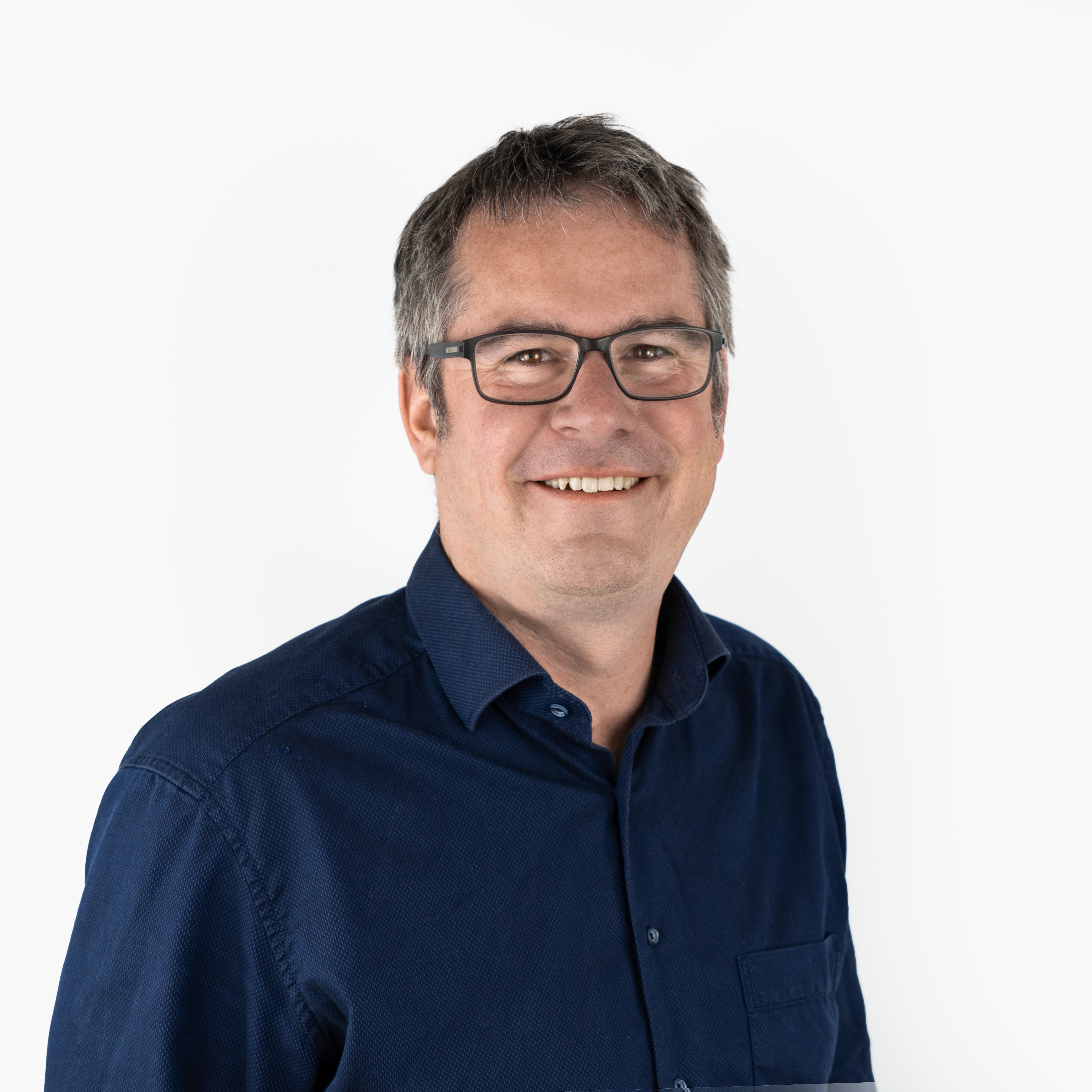 Porträt von Rechtsanwalt Matthias Mayer: Ein Mann mittleren Alters mit kurzen, grau melierten Haaren und Brille. Er trägt ein dunkelblaues Hemd und lächelt freundlich.