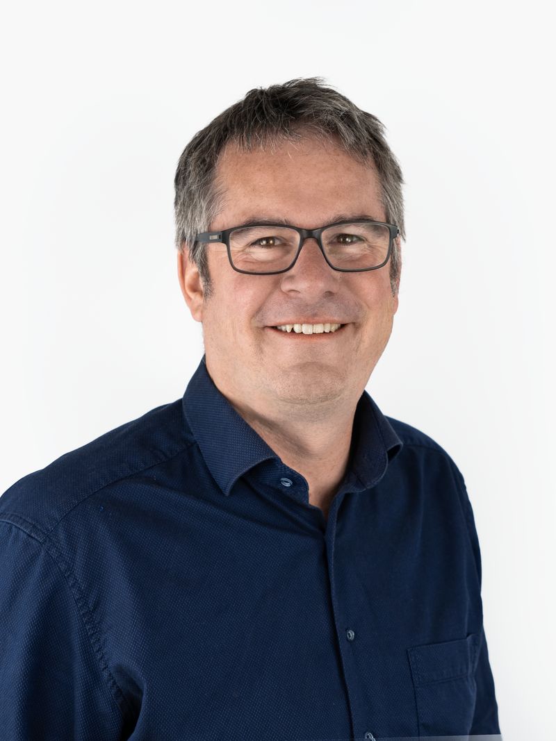 Porträt von Rechtsanwalt Matthias Mayer: Ein Mann mittleren Alters mit kurzen, grau melierten Haaren und Brille. Er trägt ein dunkelblaues Hemd und lächelt freundlich.